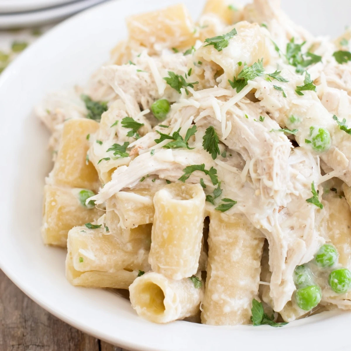 This photo shows a bubbling Slow Cooker Chicken Alfredo Pasta Bake with a rich, white sauce and herbs.