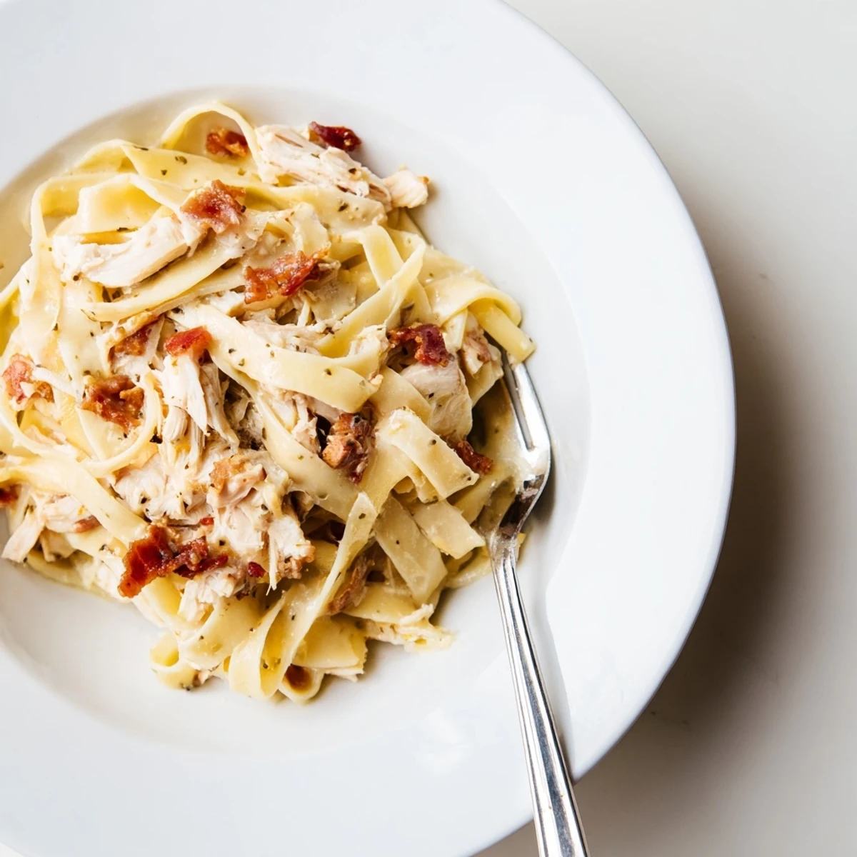 Close-up of Chicken Carbonara plated on a wooden table, garnished with fresh parsley and a generous dusting of grated Parmesan, captured in warm natural light.