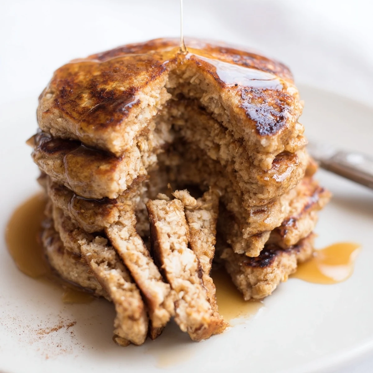 Golden-brown Banana Oat Pancakes stack high, topped with fresh banana slices and a drizzle of pure maple syrup.