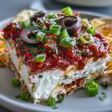Creamy 4-Way Layered Dip with refried beans and sour cream, topped with chopped tomatoes, green onions, and black olives.