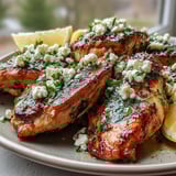 Tender slices of Greek Chicken with Lemon and Feta sizzling in a skillet with herbs and golden-brown edges.