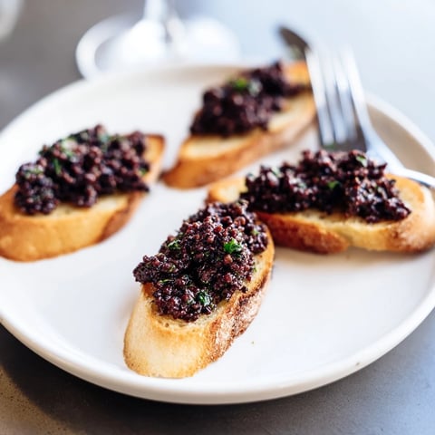 Golden, crispy baguette crostini topped with vibrant black olive tapenade, a delicious appetizer spread.
