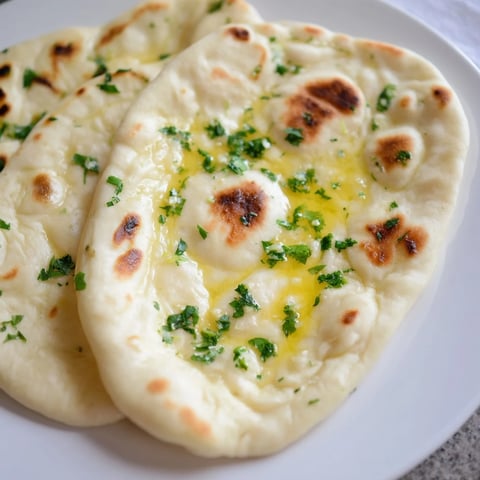 Homemade Garlic Naan, golden brown from the skillet, brushed generously with melted garlic butter and cilantro.