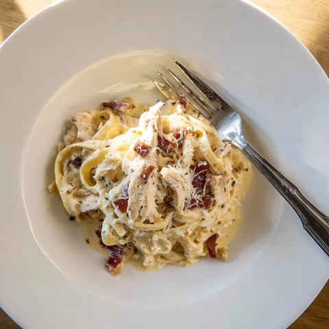 Steaming Chicken Carbonara served in a white bowl, showcasing glossy pasta strands coated in creamy egg sauce with crispy bacon bits and tender shredded chicken.