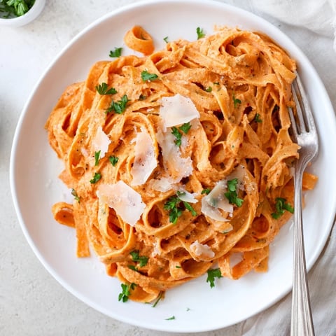 Creamy roasted red pepper pasta twirls on a fork, with vibrant red sauce clinging to penne and fresh basil garnish.