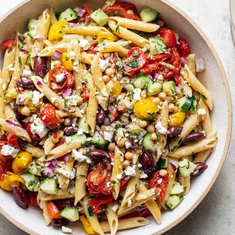 A bright bowl of Mediterranean pasta salad with chickpeas, featuring juicy tomatoes and creamy feta cheese.