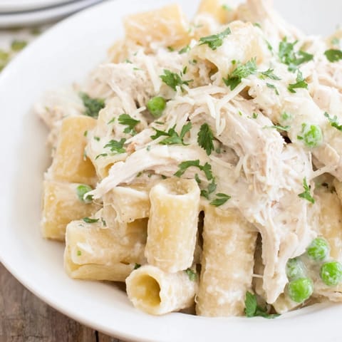 This photo shows a bubbling Slow Cooker Chicken Alfredo Pasta Bake with a rich, white sauce and herbs.