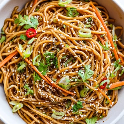 Steaming Asian Garlic Noodle Bowl in a skillet, showcasing glossy noodles coated in a rich garlic-butter sauce with julienned carrots.