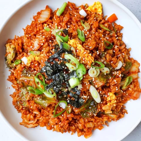 This close-up of Spicy Kimchi Fried Rice shows caramelized kimchi and vibrant vegetables sizzling in a wok, garnished with sesame seeds and fresh scallions.  