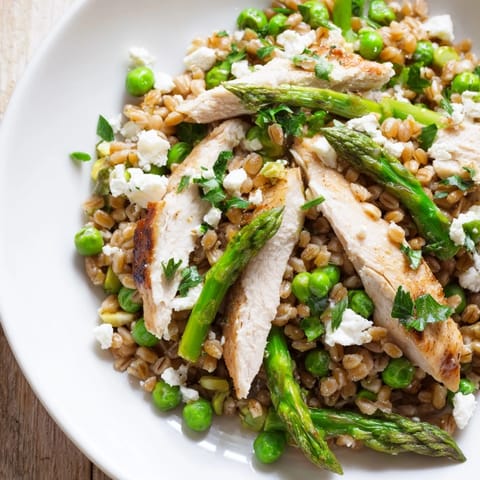 A close-up of Warm Spring Farro Chicken Salad, tossed with lemon vinaigrette and topped with crumbled feta and herbs.
