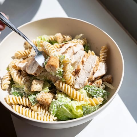 Steaming Caesar Pasta Chicken Bowl featuring al dente penne, golden chicken strips, crunchy croutons, and shaved Parmesan.