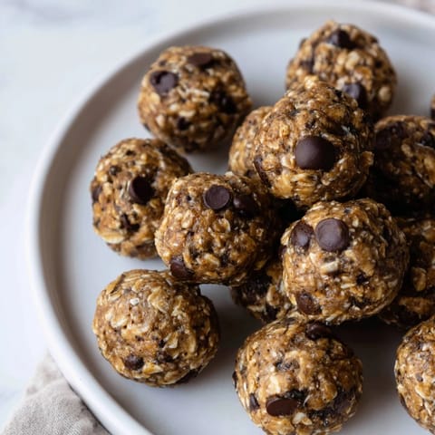 A hand reaching for Banana Chocolate Energy Balls in a small glass jar, suggesting an easy grab-and-go snack for busy U.S. mornings.