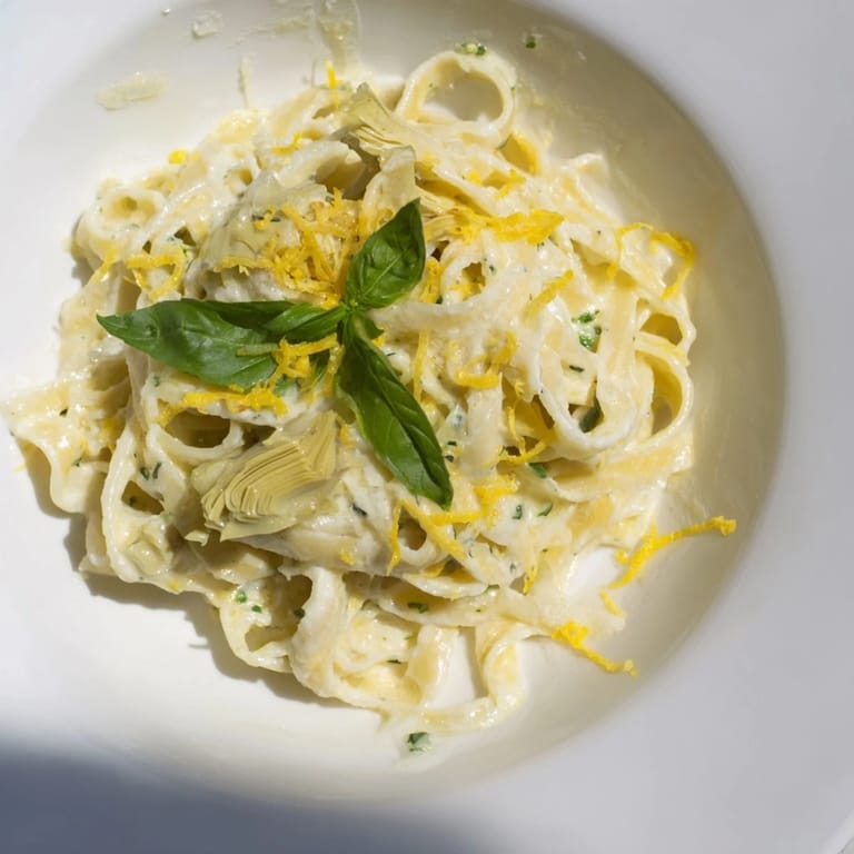 A flavorful bowl of Creamy Lemon Artichoke Pasta, served hot with a sprinkle of Parmesan cheese.