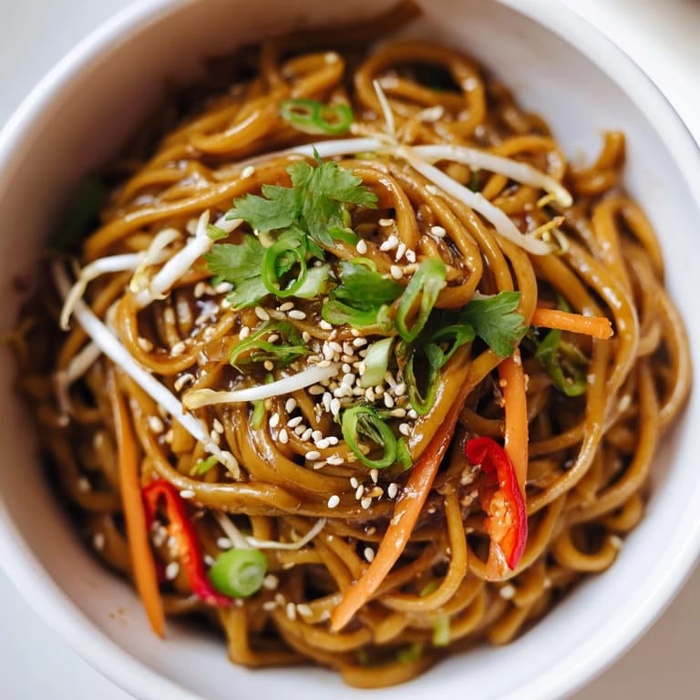 Freshly prepared Asian Garlic Noodle Bowl topped with bean sprouts, sliced red chili, and toasted sesame seeds for a vibrant finish.