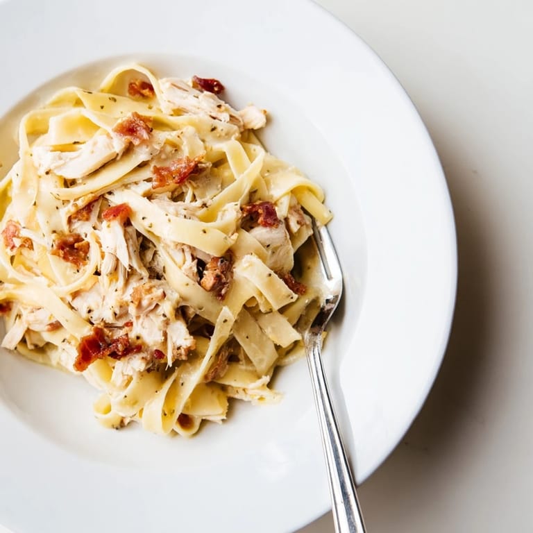 Close-up of Chicken Carbonara plated on a wooden table, garnished with fresh parsley and a generous dusting of grated Parmesan, captured in warm natural light.