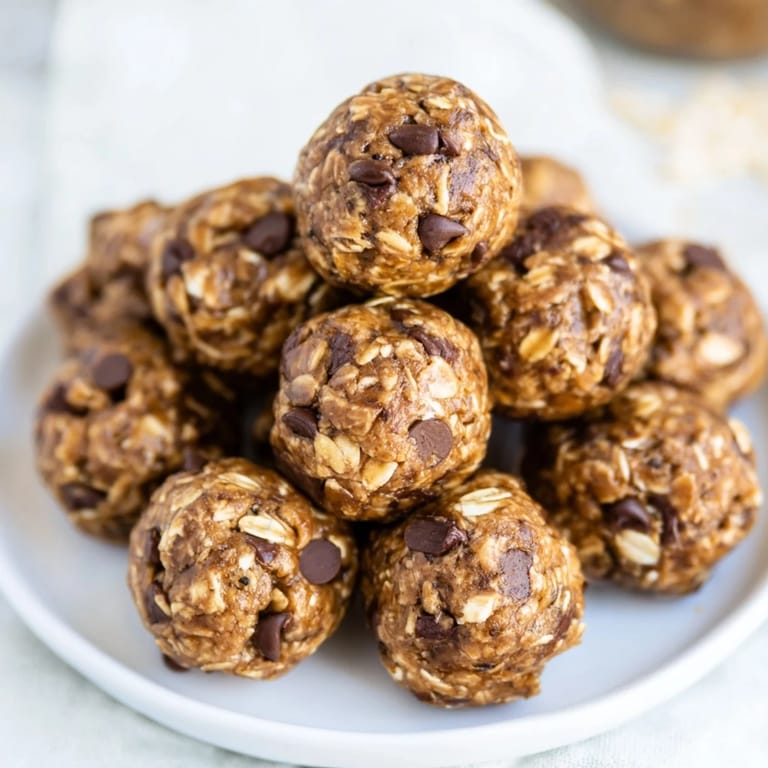 A batch of golden-brown Banana Chocolate Chip Energy Balls arranged on parchment paper, with a bowl of rolled oats and a ripe banana nearby.