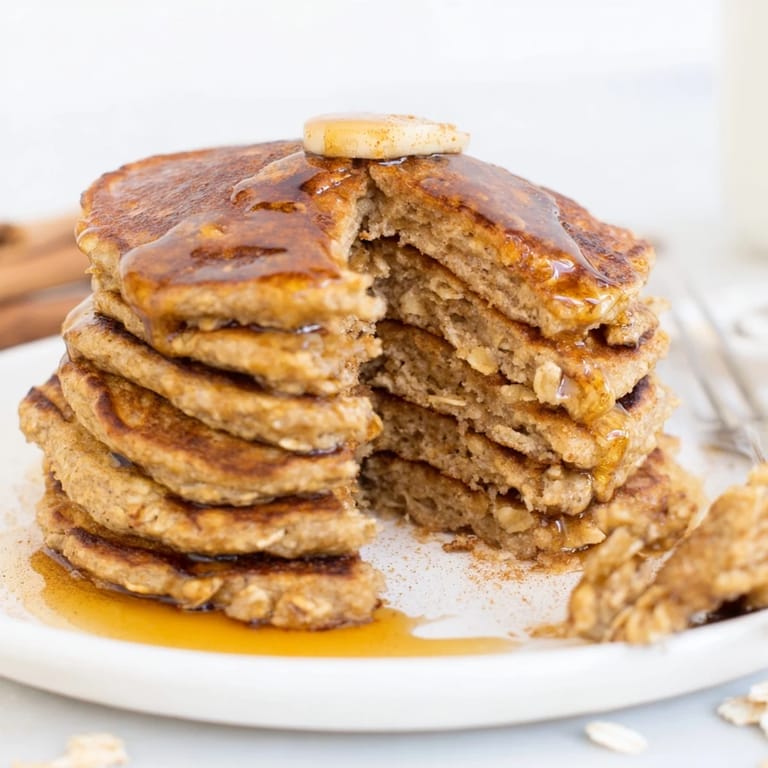 A close-up view of fluffy Banana Oat Pancakes cooking on a griddle, showing bubbling edges and a golden texture.
