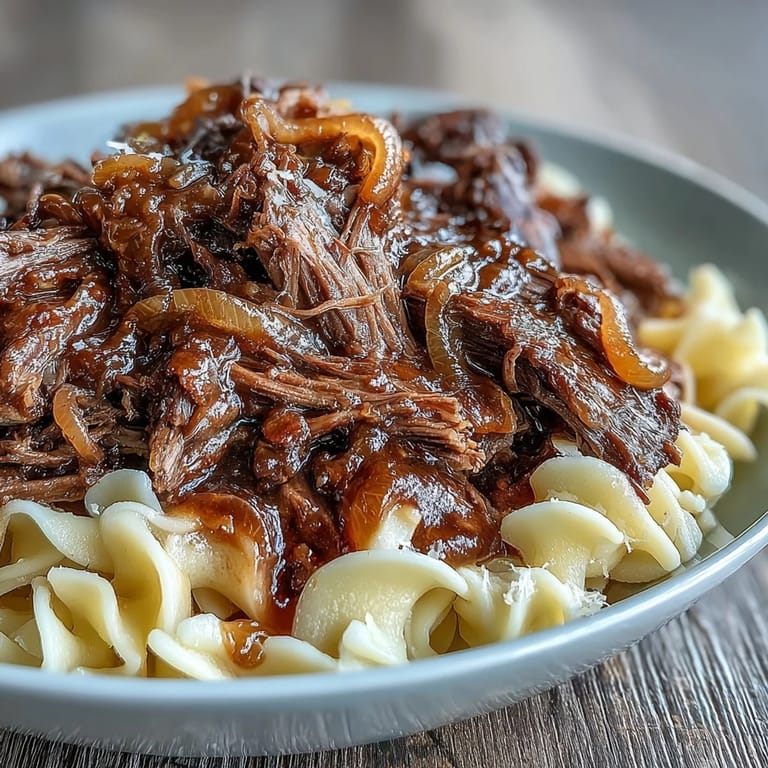 Comforting Crockpot French Onion Pot Roast Pasta served family-style, featuring caramelized onions and savory beef over noodles.